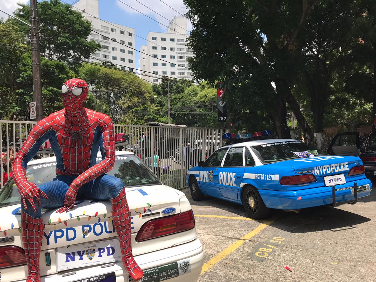 Imagem mostra homem aranha sentado em cima de capo de carro de polícia